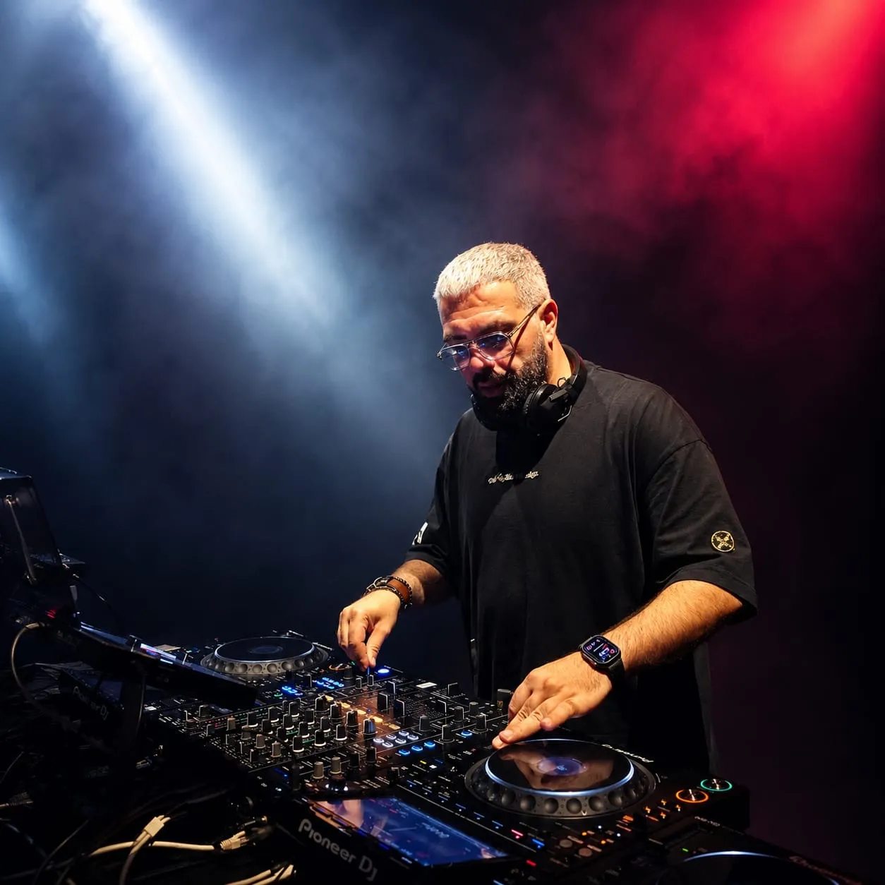 DJ in a black shirt mixing on the decks under white and red stage lights