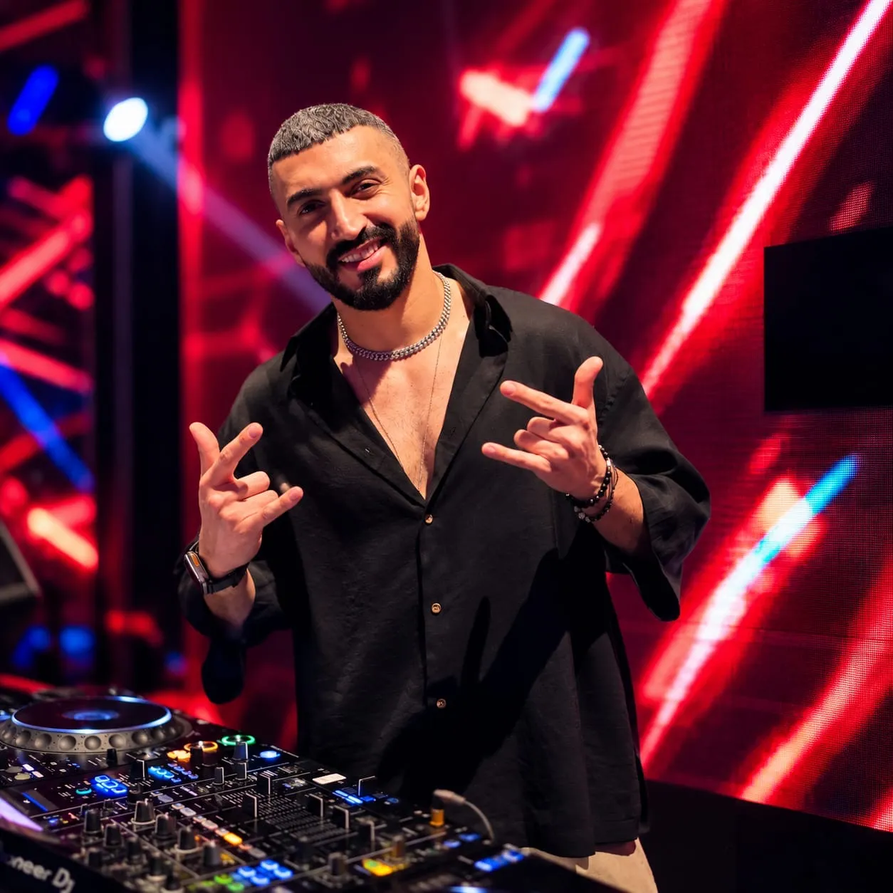 Performer in a black shirt making hand signs in front of red light panels
