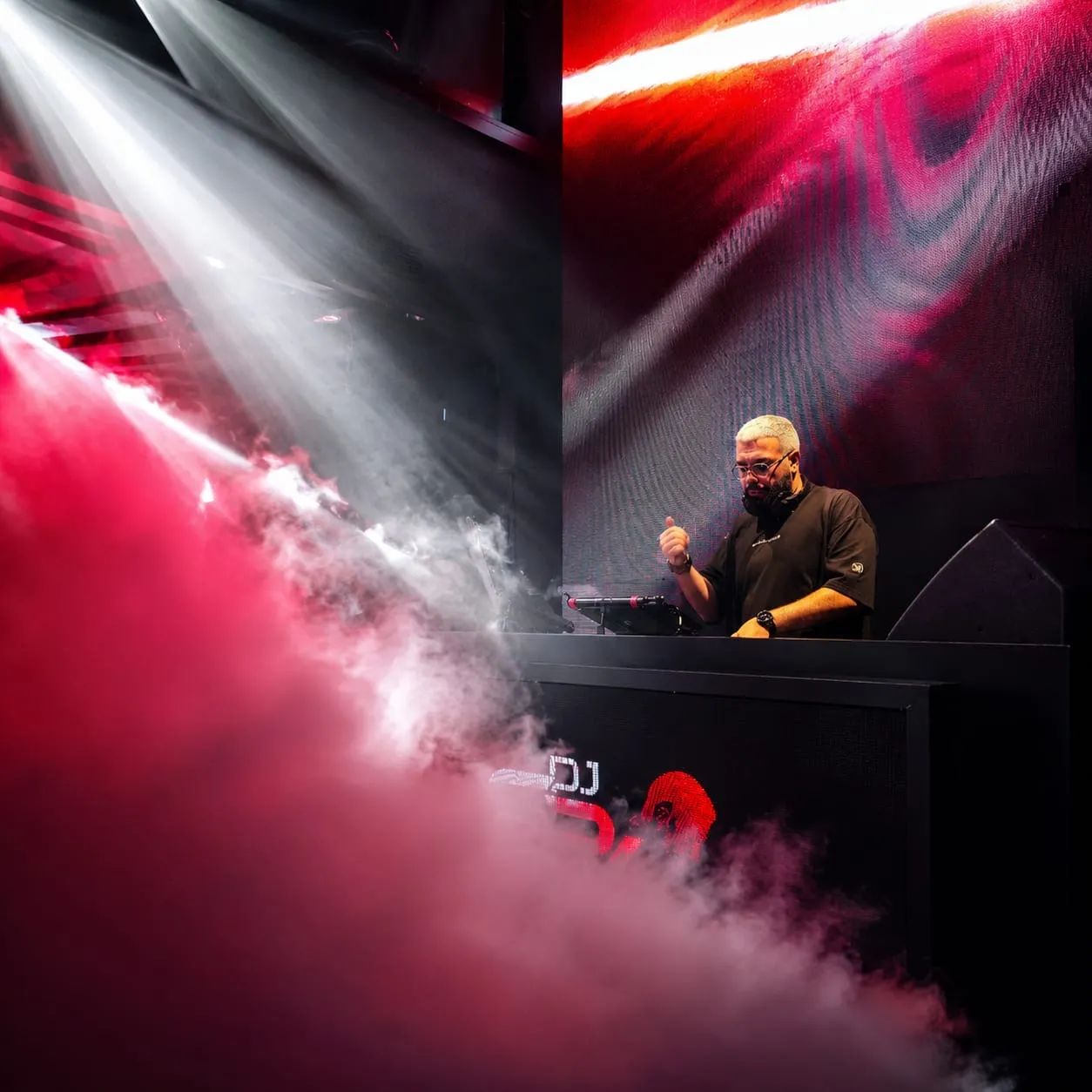 Red and white fog drifting past the DJ booth as the DJ plays