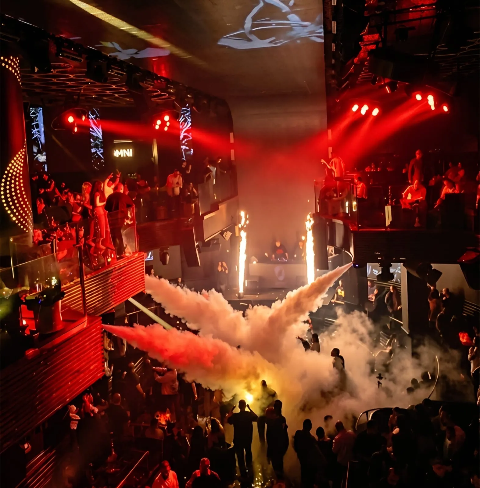 Stage fountains and red haze rising over the dance floor below tiered balconies